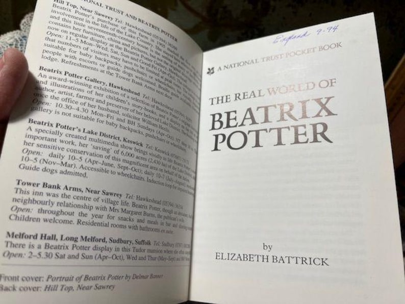 May include: Open book titled "The Real World of Beatrix Potter" by Elizabeth Battrick. The cover is white with silver lettering. The left page contains text about Beatrix Potter's life and locations.
