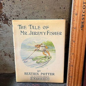 May include: A vintage book cover featuring a cartoon frog on a lily pad with the title "The Tale of Mr. Jeremy Fisher" by Beatrix Potter. The book is published by F. Warne & Co.