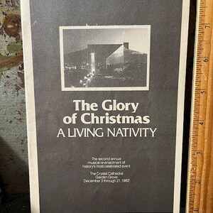 May include: A black and white poster with the text "The Glory of Christmas A Living Nativity." The poster includes a photograph of a building and text that reads "The Crystal Cathedral Garden Grove December 3 through 21, 1982."