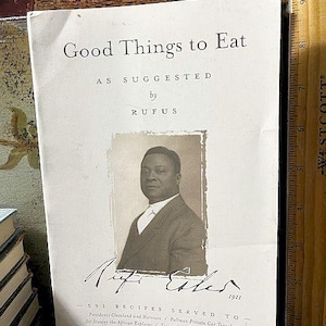 May include: A vintage cookbook titled "Good Things to Eat" with a sepia-toned portrait of a man named Rufus. The cover features text and a list of recipes served to notable figures from the late 1800s. A wooden ruler is visible on the right.