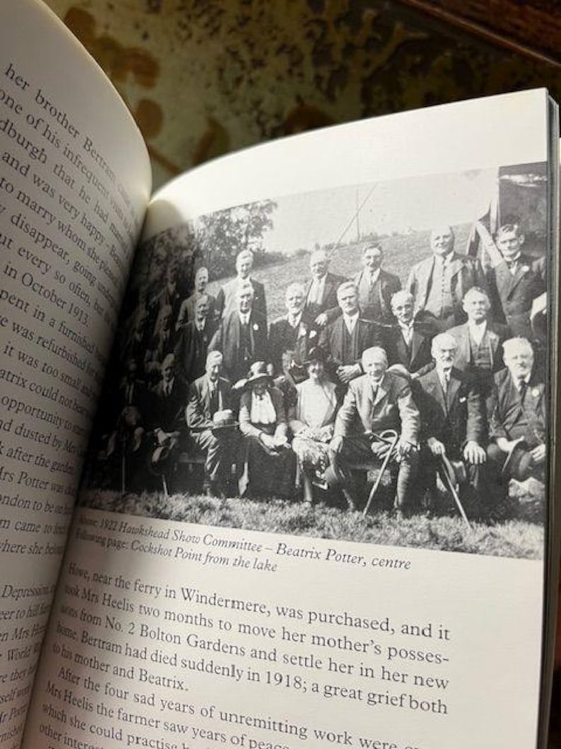 May include: A black and white photograph of the 1922 Hawkshead Show Committee, with Beatrix Potter at the center. The group of men and women are posed outdoors, some seated and others standing. The image is from a book.