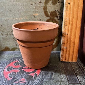 May include: A small terracotta flower pot with a rounded bottom and a slightly flared rim. The pot is empty and appears to be new.