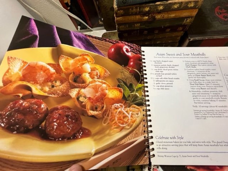 May include: A close-up of a plate of Asian sweet and sour meatballs with a side of noodles. The meatballs are served in wonton cups and are topped with a sweet and sour sauce. The recipe is printed on the page next to the plate.