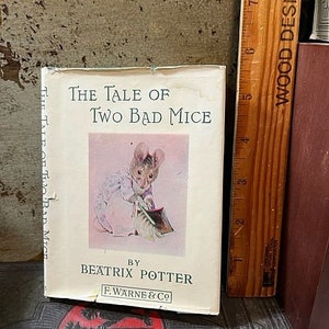 May include: A vintage book titled "The Tale of Two Bad Mice" by Beatrix Potter. The cover features an illustration of a mouse in a blue and white dress holding a broom.