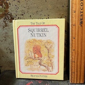 May include: A yellow book cover with the title "The Tale of Squirrel Nutkin" by Beatrix Potter. The cover features an illustration of a squirrel sitting on a branch.