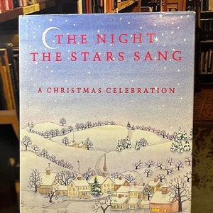 May include: A book cover with a blue background and white stars. The title is "The Night The Stars Sang" in red letters. The subtitle is "A Christmas Celebration" in black letters. The cover features a winter scene with a small village and a church.