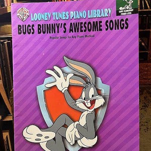 May include: A Looney Tunes piano book titled "Bugs Bunny's Awesome Songs" with Bugs Bunny on the cover. The cover is purple with a diagonal stripe pattern. The book is for early elementary primer level piano students.
