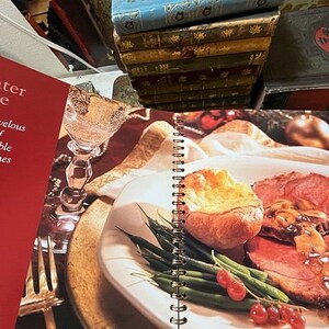 May include: A cookbook titled "Center Stage" with a red cover and the text "A marvelous menu of memorable main dishes and more". The book is open to a page showing a plate of roast beef with Yorkshire pudding, green beans, and red currants.