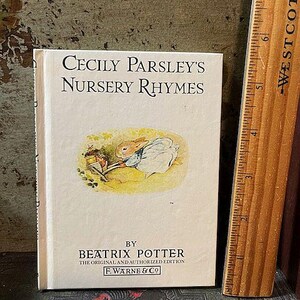 May include: A vintage book titled "Cecily Parsley's Nursery Rhymes" by Beatrix Potter. The book features a colorful illustration of a rabbit sitting on a rock with a book in its lap.