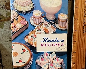 May include: A vintage cookbook featuring Knudsen Dairy Products recipes. The cover features a colorful spread of food, including a pink and white dessert, a green salad, and a bowl of creamy white pudding. The text "Knudsen Recipes" is printed in bold, black letters.