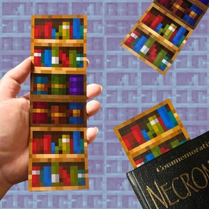 May include: A Minecraft-themed bookmark featuring a bookshelf with multiple rows of colourful books. The bookmark is made of paper and has a pixelated design.