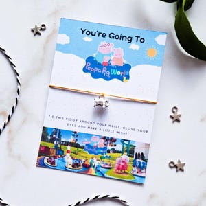 May include: A gold string bracelet with a silver charm, presented on a card with the text "You're Going To Peppa Pig World". The card features Peppa Pig characters and a theme park image, with star-shaped charms scattered around.