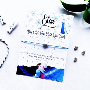 Könnte beinhalten: Eine blaue und weiße Karte mit einem Bild von Elsa aus Frozen. Die Karte sagt "Elsa Lass dich von der Angst nicht zurückhalten" und "Binde dieses Herz um dein Handgelenk, schließe deine Augen und wünsch dir etwas! Liebe: Elsa x".