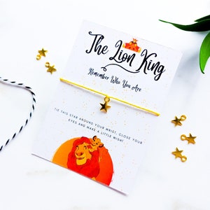 May include: A yellow string bracelet with a gold star charm. The bracelet comes with a card that says "The Lion King" and "Remember Who You Are." The card also features a cartoon image of Simba and Mufasa from the Disney movie.
