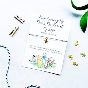 May include: A gold star charm bracelet with a white card that says "Keep Looking Up That's The Secret Of Life Winnie The Pooh" and a picture of Winnie the Pooh and his friends.