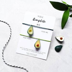 May include: Two avocado-shaped friendship bracelets with green and yellow string. The bracelets are tied together with a card that says "You Complete Me" and "Let's tie these avocado's around our wrists so that we will always be complete! Close your eyes and make a little wish!"