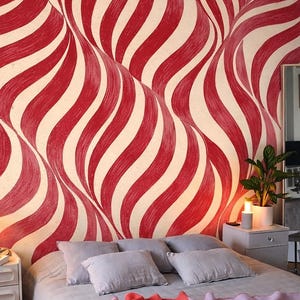 Può includere: Camera da letto con carta da parati a motivi ondulati rossi e crema. Il letto ha cuscini grigi e una coperta con sezioni rosse e lavanda. Una lampada argentata è su un comodino bianco. Il pavimento è in legno.