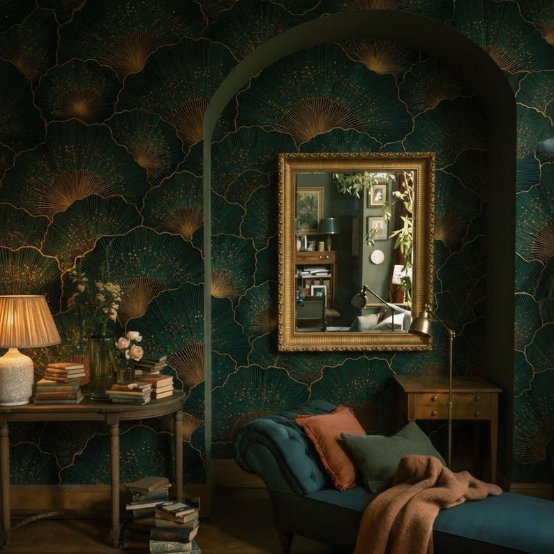 May include: An interior scene featuring a dark green wallpaper with a gold fan-like pattern. A gold-framed mirror hangs on the wall, reflecting a room with a desk and plants. A teal chaise lounge with orange and green pillows sits in the foreground.