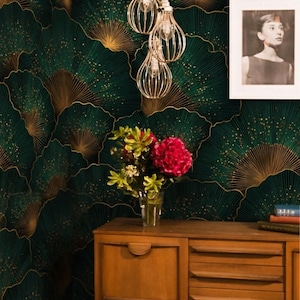 May include: A room with a dark green and gold fan-patterned wallpaper. A wooden cabinet holds a vase of flowers and a framed black and white photo. Decorative light fixtures hang from the ceiling.