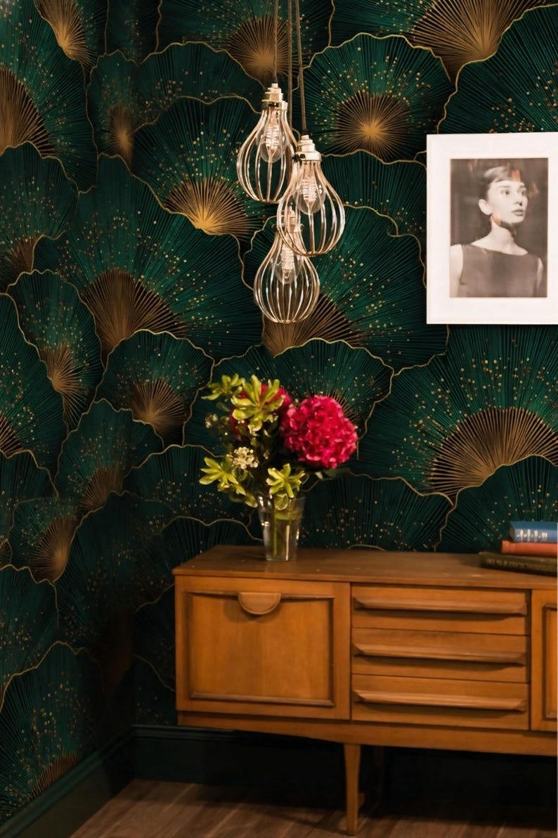 May include: A room with a dark green and gold fan-patterned wallpaper. A wooden cabinet holds a vase of flowers and a framed black and white photo. Decorative light fixtures hang from the ceiling.
