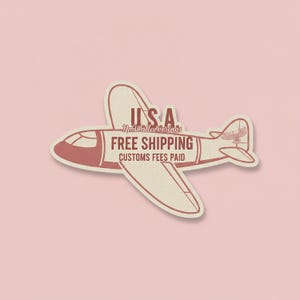 May include: A sticker in the shape of a vintage airplane with the text "USA" and "Free Shipping" in a retro font. The airplane is cream-colored with red accents and a pink background.