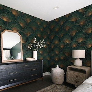 May include: A bedroom with dark green and gold patterned wallpaper. A black dresser with gold hardware and a wooden-framed mirror are against the wall. A white lamp sits on a wooden nightstand next to a bed with a gray headboard.