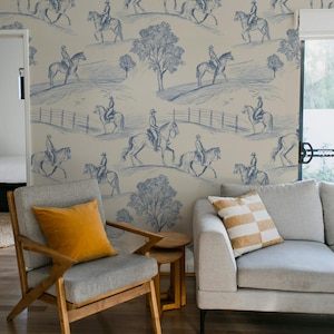 May include: A room with wallpaper depicting a blue and white equestrian design. A gray armchair with a yellow cushion, a small wooden side table, and a gray sofa with a striped cushion are in front of the wallpaper.