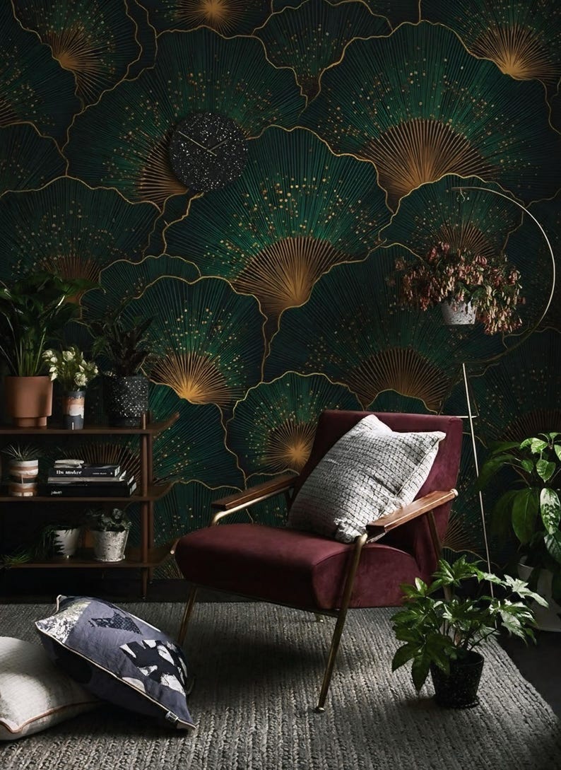 May include: A stylish living room with a dark green and gold patterned wallpaper. A burgundy armchair with a gray pillow sits in front of the wall. Potted plants and a small bookshelf add to the decor.