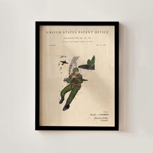 May include: Framed patent print featuring a diagram of a military combat system. The illustration depicts a soldier in green uniform with a parachute, a plane, and the text "United States Patent Office". The print has a vintage aesthetic.