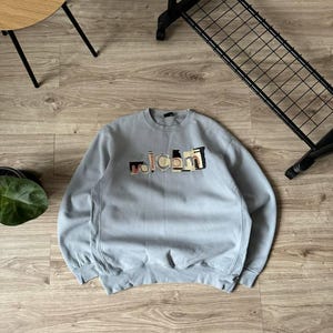 May include: A light blue sweatshirt with a multi-colored "Volcom" logo printed on the front.