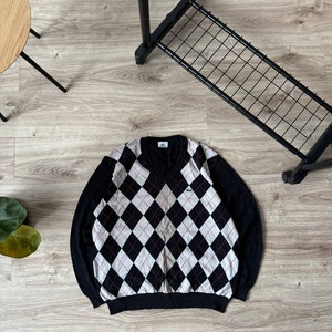 May include: Black and white argyle patterned sweater with a v-neck and a small crocodile logo on the chest.