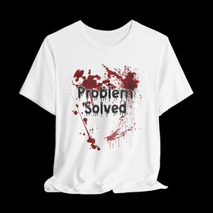 Könnte beinhalten: Weißes T-Shirt mit dem schwarzen Schriftzug "Problem Solved" und roten Spritzern. Das Shirt besteht aus einem weichen Material und hat einen klassischen Rundhalsausschnitt.