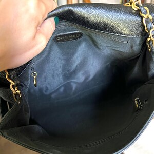 May include: Black leather handbag with gold chain straps. The interior is black with a small zippered pocket and a gold-toned charm. The brand name "CHANEL" is visible inside the bag.