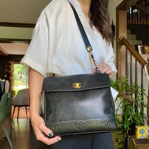 May include: Black leather shoulder bag with a gold-tone clasp and chain strap. The bag features embossed interlocking Cs on the front and a flap closure. The bag is carried by a black strap with gold chain accents.