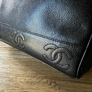 May include: Close-up of a black leather handbag with a textured surface. The bag features embossed interlocking double C logos along the bottom edge, a signature design element.