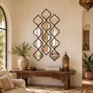 Peut inclure: Un miroir mural composé d'un agencement vertical de dix panneaux de verre en forme de quatre-feuilles interconnectés, encadrés de métal noir. Le design crée un motif géométrique répétitif qui reflète l'intérieur de la pièce.