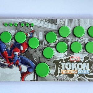 Może przedstawiać: Niestandardowy układ przycisków do gier z grafiką Spider-Mana. Projekt zawiera czarno-białe tło i zielone przyciski. Tekst "MARVEL TOKON FIGHTING SOULS" jest widoczny w prawym dolnym rogu.