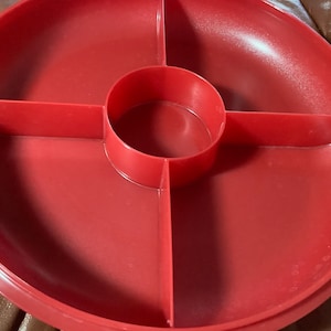 May include: A red plastic serving platter with a circular shape and four divided sections. The center has a raised circular compartment. The platter is designed for serving snacks or appetizers.