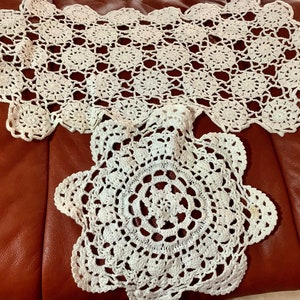 May include: Two handmade, off-white crochet doilies. One is rectangular with a scalloped edge and a repeating floral pattern. The other is round with a similar floral design and scalloped edge. Both are on a brown surface.