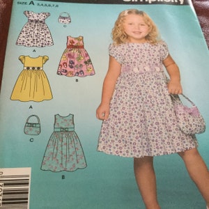 May include: A young girl in a floral print dress with a matching purse. The dress has a purple floral pattern and a lilac sash. The image also shows dress patterns with different designs and a size chart.