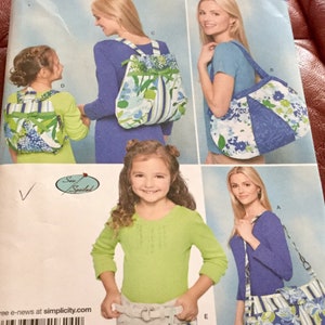 May include: Simplicity sewing pattern featuring various bag designs. The bags showcase a floral pattern with blue, white, and green hues. The pattern includes backpacks, tote bags, and a small purse, all with coordinating fabric.