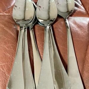 May include: A collection of shiny, stainless steel spoons. The spoons have a teardrop-shaped bowl and a long, slender handle. The spoons are arranged in a close-up shot, with the light reflecting off their polished surfaces.