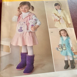 May include: Simplicity pattern 1288 A featuring children's clothing designs. The main image shows a girl in a pink dress with cat appliqués, purple boots, and a stuffed cat. Additional designs include a yellow hooded outfit and a blue dress with bear appliqués.