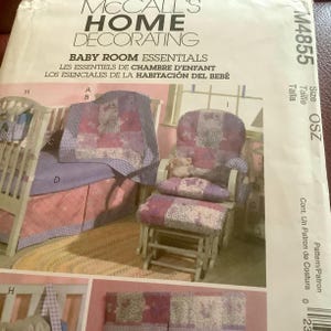 May include: A McCall's Home Decorating pattern for baby room essentials. The image shows a crib, a rocking chair, and a footstool, all with matching pink and purple floral fabric. The pattern includes instructions for making baby bedding.