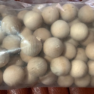 May include: A clear plastic bag filled with numerous unfinished wooden spheres. The spheres are a light beige color, and appear to be made of raw wood. The spheres are of various sizes and are tightly packed together.