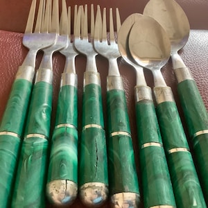 May include: A set of vintage silverware with stainless steel forks and spoons. The handles are a marbled green color with silver-toned metal accents. The set includes multiple forks and spoons, ideal for a formal dining setting.