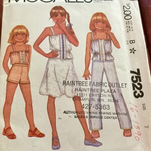 May include: McCall's sewing pattern envelope featuring illustrations of girls' outfits: shorts set, dress, and pantsuit. The envelope includes the text "RAINTREE FABRIC OUTLET" and the pattern number 7523.