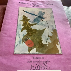 May include: A craft pattern titled "Blowing In The Wind" featuring a dragonfly, ladybug, and leaves. The artwork is 18 inches by 27 inches. The design is by Ruth Carolyn Miller.
