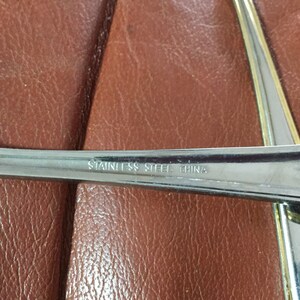 May include: Close-up of stainless steel silverware with the text "STAINLESS STEEL CHINA" etched on the handle. The silverware is set against a brown leather surface.