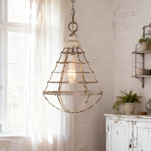 Puede incluir: Una lámpara colgante de estilo vintage con una pantalla de cristal transparente encerrada en una jaula de metal envejecido. La luz cuelga de una cadena y presenta una bombilla visible. La lámpara está suspendida en una habitación con una pared blanca y una ventana.